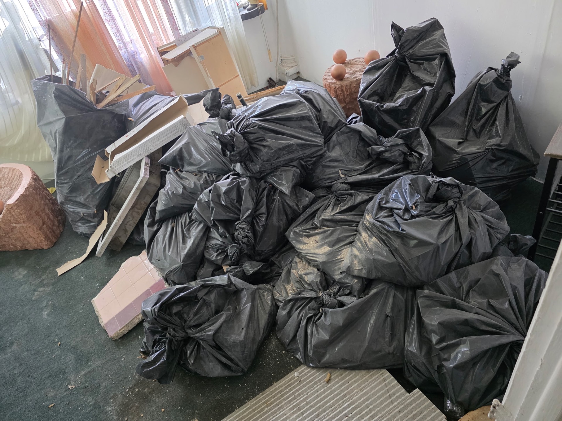 Room packed with dozens of black contractor bags, lumber and tile scrap before B.L.O.O.M. Entity cleanout